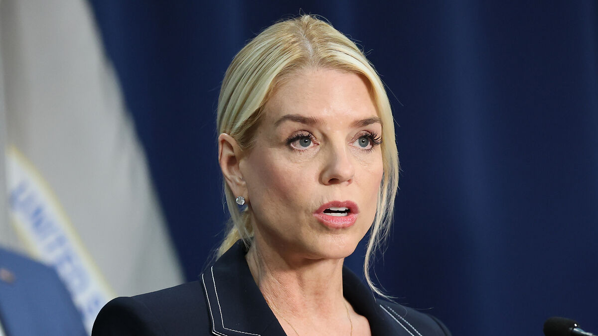 Pam Bondi speaking seriously at a press event, with focused expression and blue backdrop behind her.
