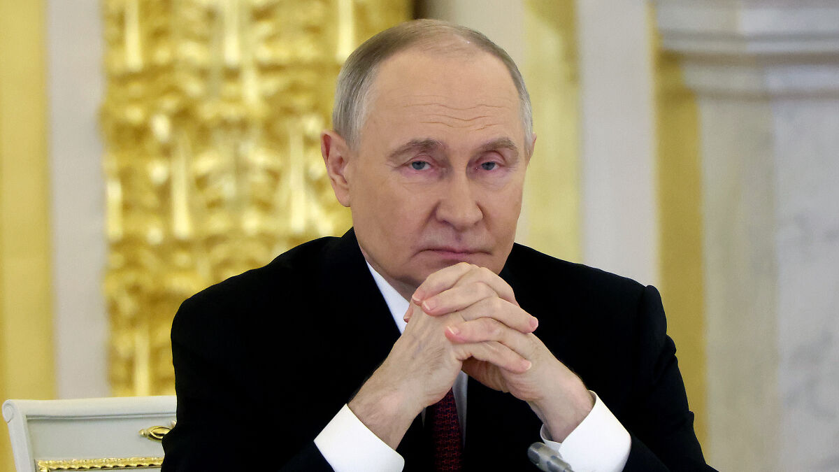 A serious man in a black suit sitting with hands clasped, related to hungover Russians and Ukraine secret deep strike plan.