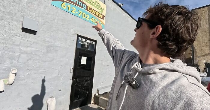 Man in a gray hoodie pointing at a Minnesota child care center sign, highlighting child care funds and fraud issues. Man in a gray hoodie pointing at a Minnesota child care center sign, highlighting child care funds and fraud issues.