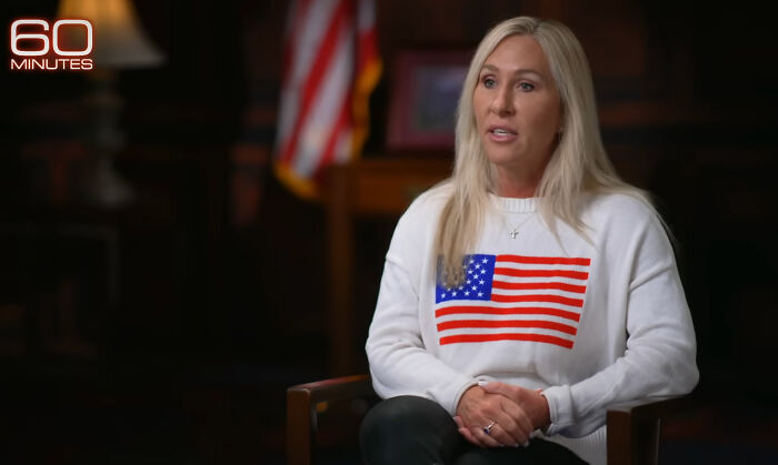 Marjorie Taylor Greene in a 60 Minutes interview, wearing a white shirt with American flag discussing Republicans and Trump.