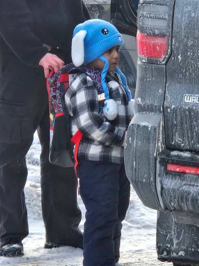 Five-year-old boy wearing a blue winter hat and backpack stands near a vehicle after being detained by ICE agents.