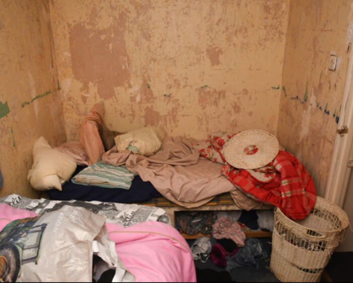 Cluttered small room with worn mattress, blankets, and laundry basket showing harsh conditions of vulnerable woman imprisoned. Cluttered small room with worn mattress, blankets, and laundry basket showing harsh conditions of vulnerable woman imprisoned.
