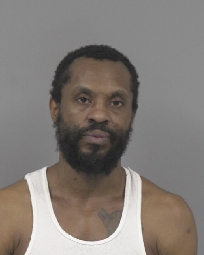 Man with beard and white tank top in a mugshot related to father allegedly hiding children&rsquo;s bodies while bringing Grindr dates home.