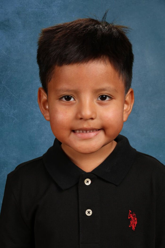 Young boy in a black polo shirt smiling against a blue backdrop, related to ICE detaining preschool child incident in Minneapolis.