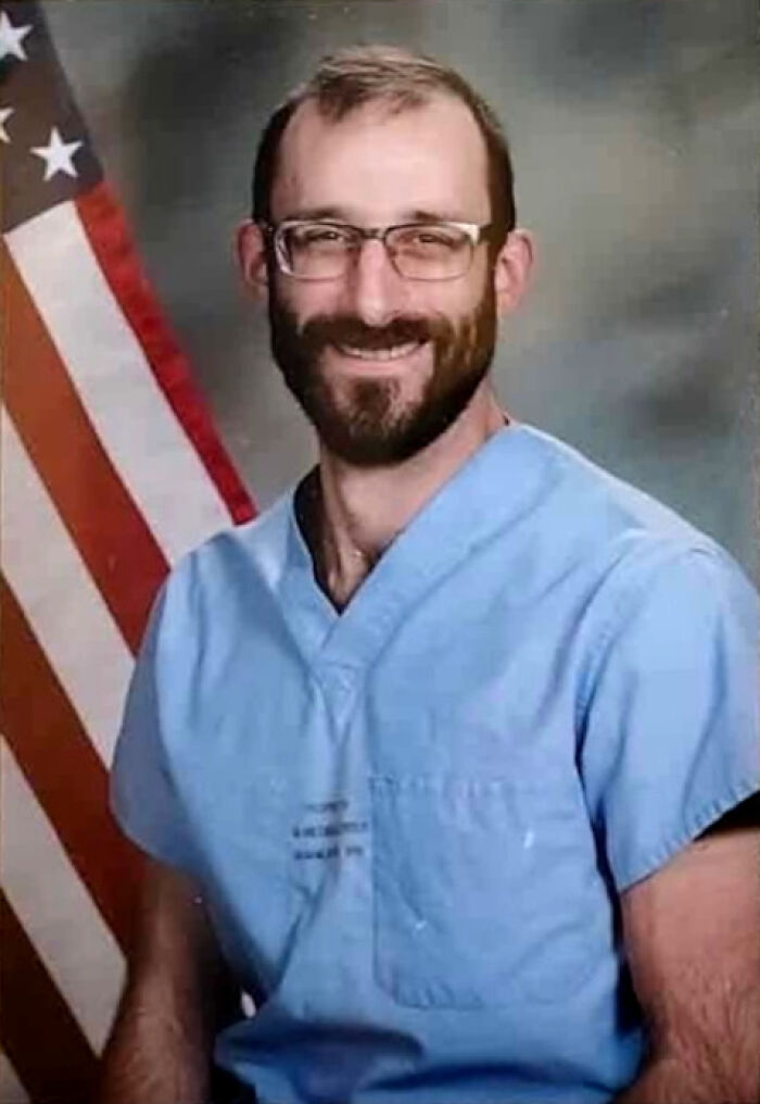 Alex Pretti wearing glasses and scrubs, smiling in front of an American flag in a formal portrait setting.