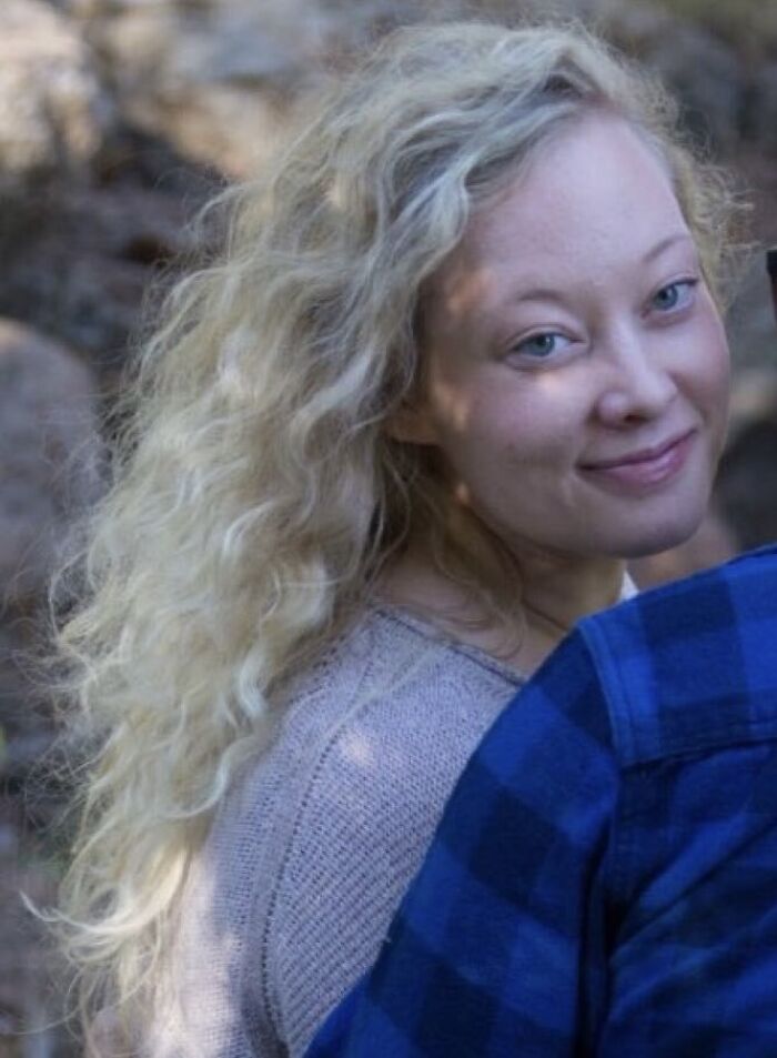 Young woman with long curly blonde hair smiling softly outdoors in natural light, unrelated to Minnesota ICE slaying discussion.