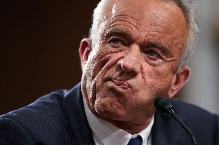 Man in a suit at a press conference with a serious expression as RFK Jr.’s ringtone interrupts the event Man in a suit at a press conference with a serious expression as RFK Jr.’s ringtone interrupts the event