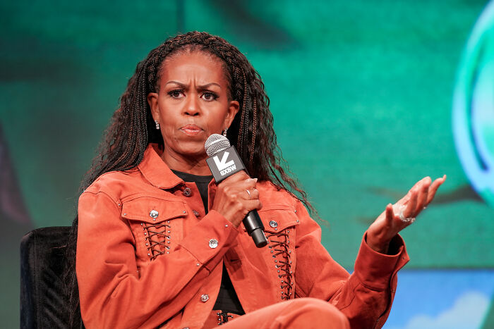 Michelle Obama speaking at an event, holding a microphone, reacting seriously during a discussion on political issues.