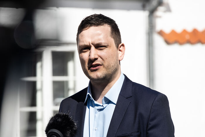 Man in navy suit speaking outdoors with microphone, related to Trump issues Greenland deadline and PM response.