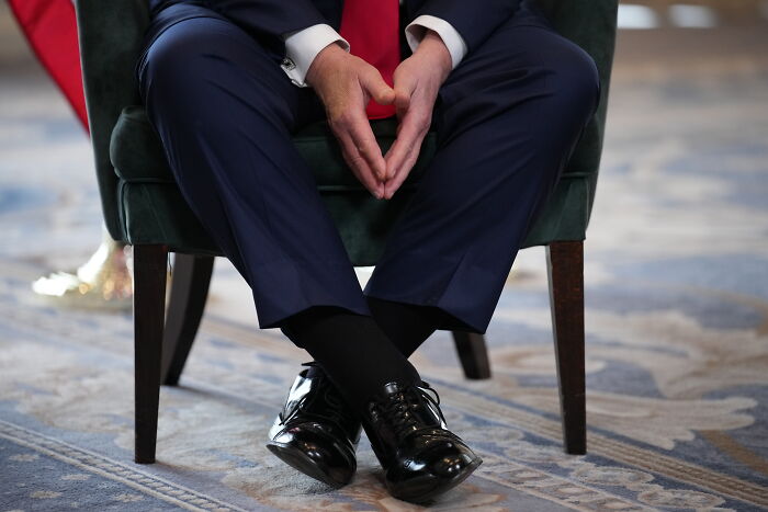 Man sitting cross-legged in polished black shoes and dark compression socks, wearing a navy suit and red tie, health-related. Man sitting cross-legged in polished black shoes and dark compression socks, wearing a navy suit and red tie, health-related.