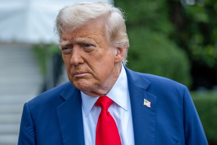 Former President Donald Trump wearing a blue suit and red tie, reflecting on being American after Trump's second year.