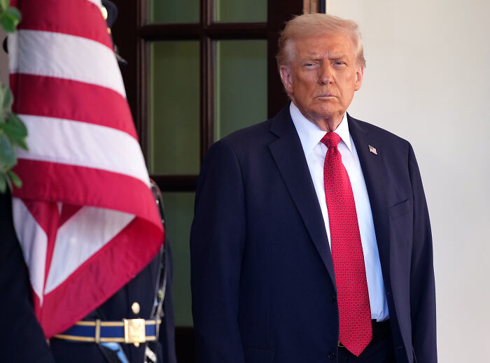 Man in navy suit and red tie standing beside U.S. flag, NYT Pulitzer mentioned Man in navy suit and red tie standing beside U.S. flag, NYT Pulitzer mentioned