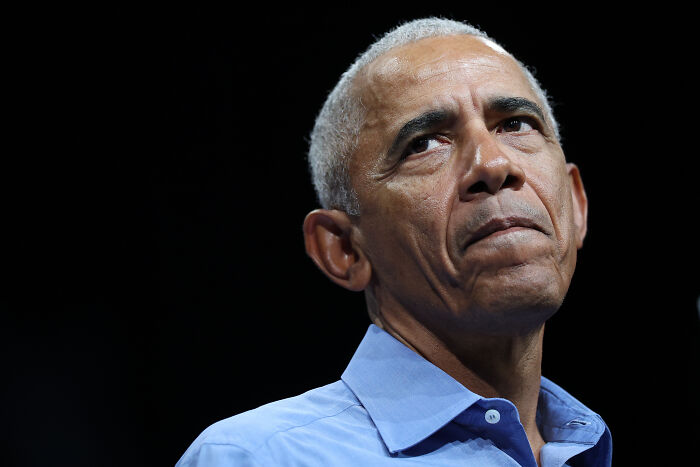 Barack Obama in a blue shirt with a serious expression, addressing a wake-up call to every American in rare statement.