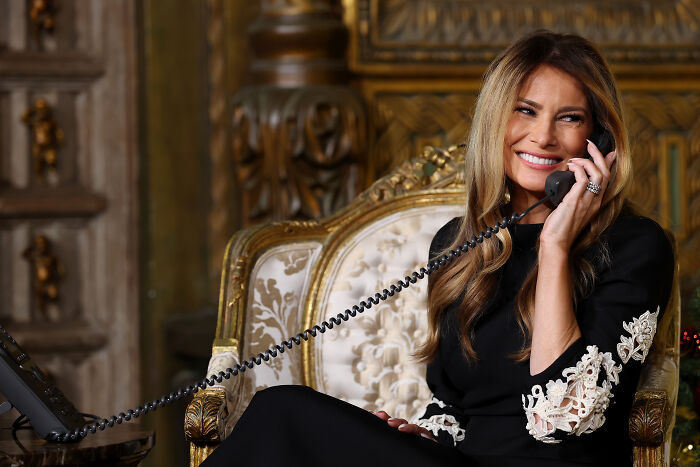 Melania Trump sitting in ornate chair smiling while talking on a black corded phone during documentary screening event. Melania Trump sitting in ornate chair smiling while talking on a black corded phone during documentary screening event.