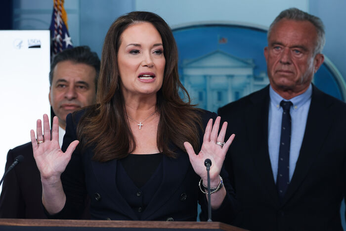 Secretary of Agriculture speaking at a podium with raised hands during a press briefing about a $3 meal proposal.