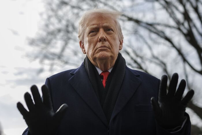Former President Trump outdoors at Davos, wearing a dark coat and gloves, with a serious expression and raised hands. Former President Trump outdoors at Davos, wearing a dark coat and gloves, with a serious expression and raised hands.
