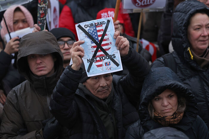 Crowd holding a crossed-out American flag sign protesting, illustrating the viral Greenland Reddit post telling Americans to stop apologizing. Crowd holding a crossed-out American flag sign protesting, illustrating the viral Greenland Reddit post telling Americans to stop apologizing.
