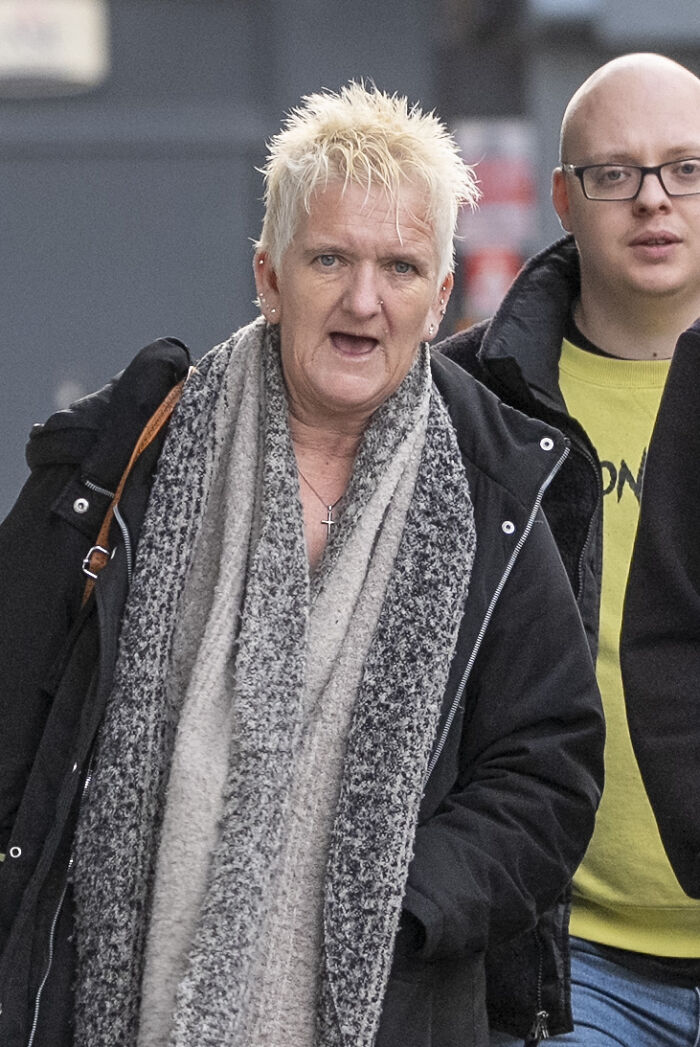Woman vulnerable and imprisoned, wearing a gray scarf and black coat, walking outdoors during daytime. Woman vulnerable and imprisoned, wearing a gray scarf and black coat, walking outdoors during daytime.