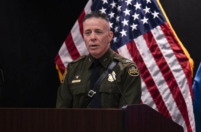 Border Patrol Chief Greg Bovino in uniform speaking at a podium with an American flag backdrop. Border Patrol Chief Greg Bovino in uniform speaking at a podium with an American flag backdrop.