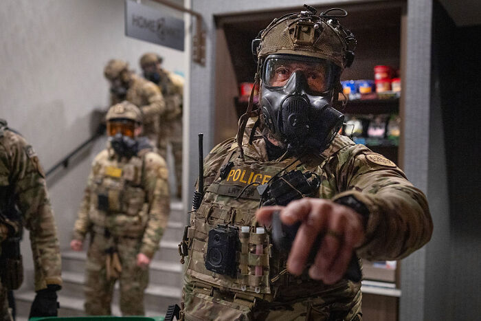 Police officer in tactical gear and gas mask pointing forward during an operation highlighting 2nd Amendment hypocrisy debate. Police officer in tactical gear and gas mask pointing forward during an operation highlighting 2nd Amendment hypocrisy debate.