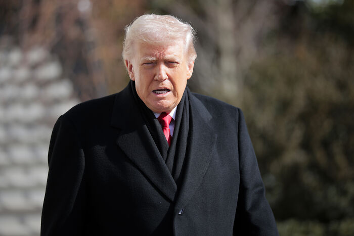 Donald Trump outdoors wearing a black coat, related to cult of personality and empathy toward shooting victims.