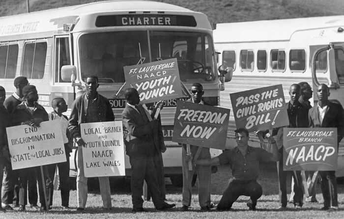 Protesters holding signs demanding civil rights bill and ending discrimination near a charter bus during a civil rights rally.