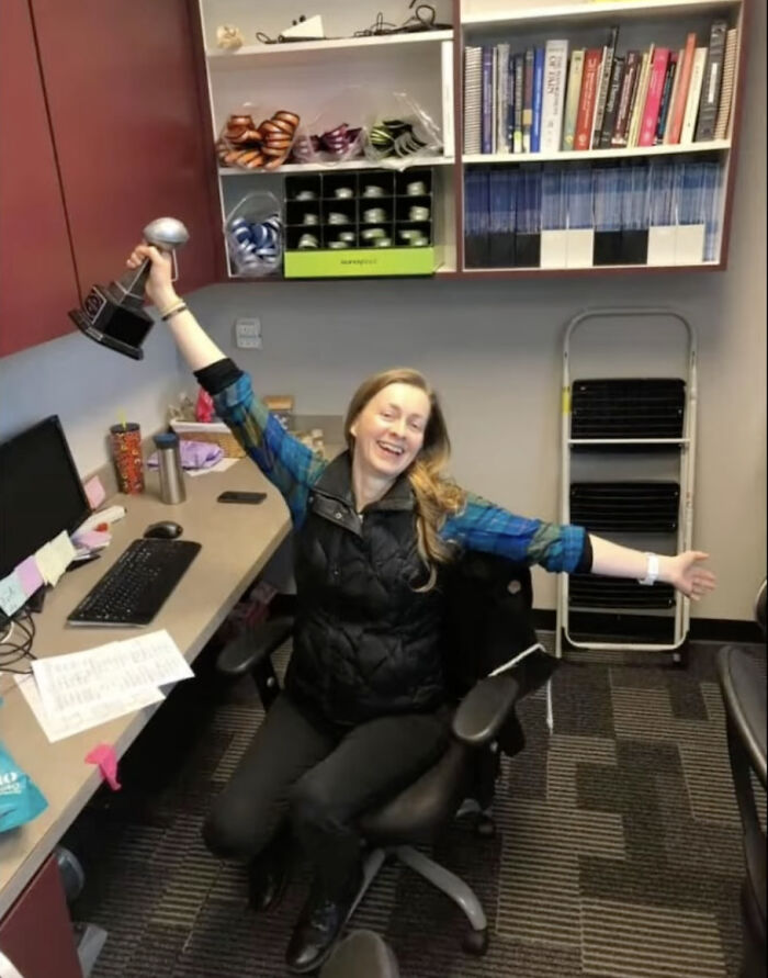 Artist mom smiling and holding up a trophy while sitting in an office chair with arms outstretched.