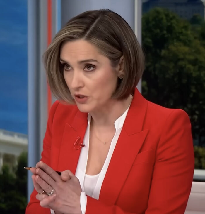 Reporter in a red blazer speaking seriously during an interview about Kristi Noem's reaction to a controversial name.