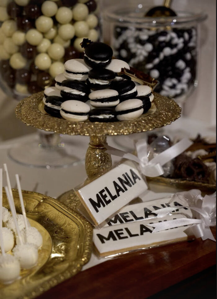 Black and white macarons on a gold stand with Melania-themed cookies displayed on a dessert table at a screening event. Black and white macarons on a gold stand with Melania-themed cookies displayed on a dessert table at a screening event.