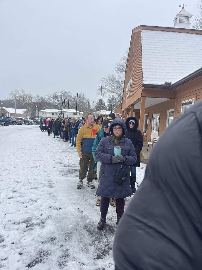 People bundled in winter jackets standing in line outside a bakery amid anti-ICE cookie controversy.