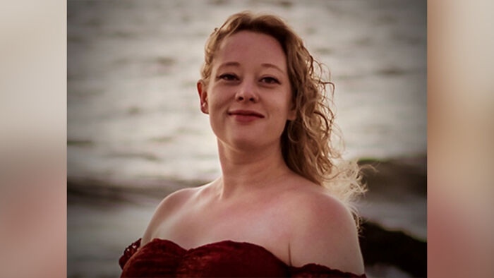 Woman with curly blonde hair in a red off-shoulder dress by the water, related to ICE agent shooting Renee Nicole Good case