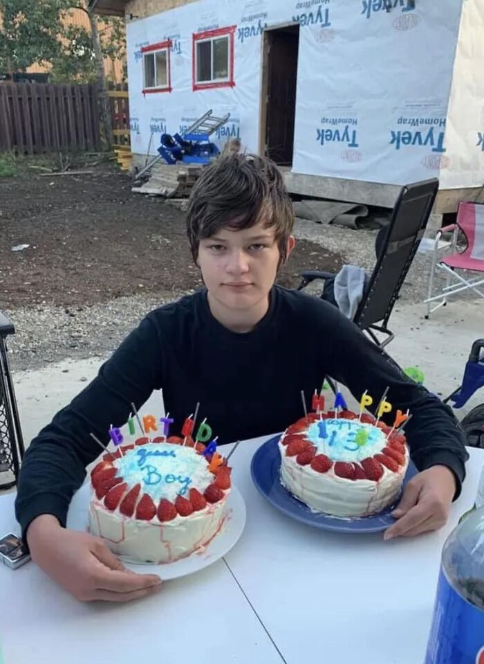 Teen boy holding two birthday cakes outside a house under construction, honoring children lost in Canada school attack.