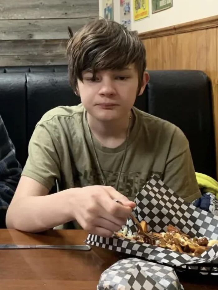 Teen boy sitting at a table eating food while families honor children lost in Canada school attack.