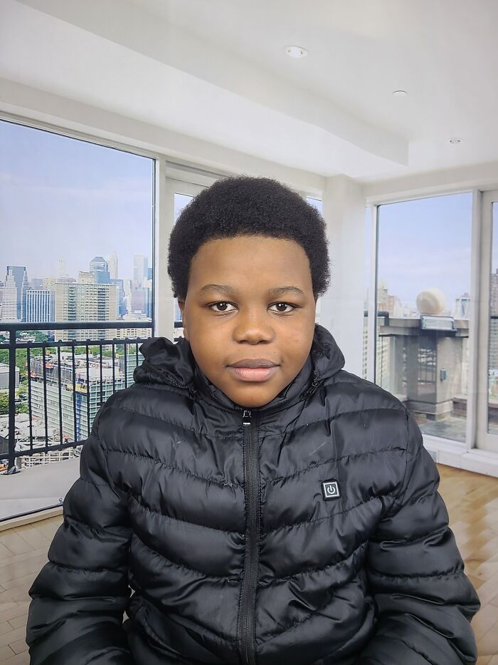 Young boy wearing a black jacket indoors with a cityscape background, representing families honoring children lost in Canada school attack.