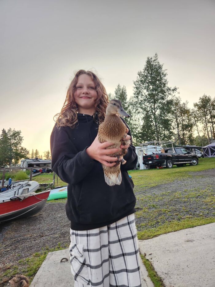 Child holding a duck outdoors as families honor children lost in Canada school attack in a peaceful setting.