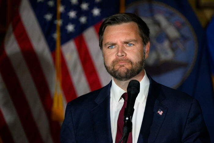 Man in suit speaking at microphone with American flags in the background, referencing White House 2028 run news. Man in suit speaking at microphone with American flags in the background, referencing White House 2028 run news.
