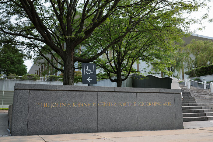 The Kennedy Center entrance with trees and a sign indicating wheelchair accessibility for repairs closure. The Kennedy Center entrance with trees and a sign indicating wheelchair accessibility for repairs closure.