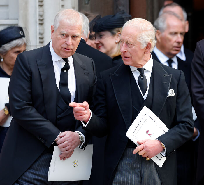 King Charles in formal attire engaged in conversation amid a group, highlighting reputation concerns in Andrew Epstein scandal.
