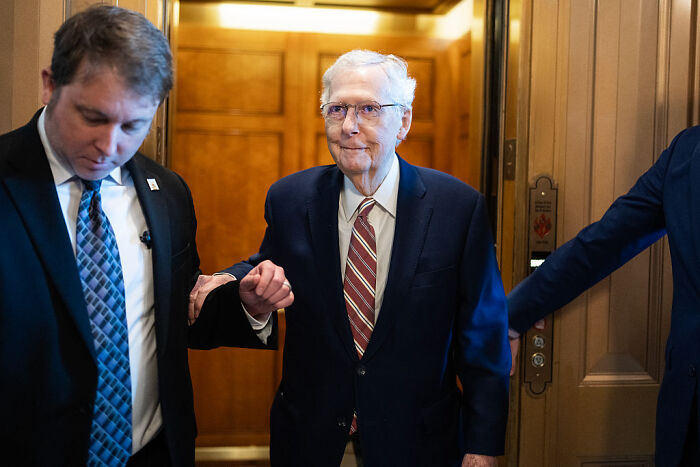 Senator Mitch McConnell, 83, in a suit and striped tie, walking with aides amid renewed term limit debate.