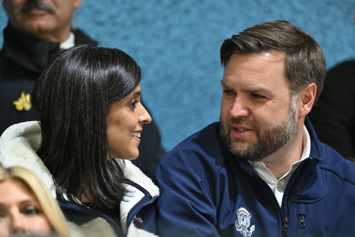 JD Vance talking to a woman, wearing a navy jacket, in a candid moment during a public event.