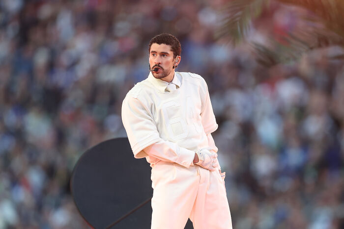 Bad Bunny performing live at a stadium event, captured mid-move with a headset microphone and white outfit.