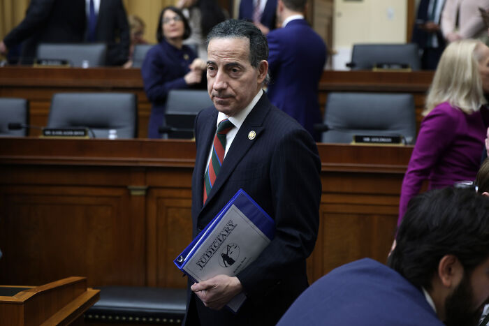 Man in a suit holding document folder in a congressional hearing room amid a tense moment involving Bondi and House Democrats.
