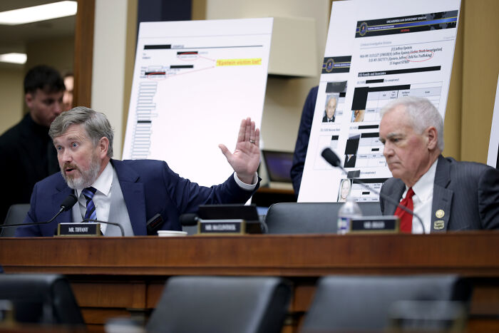 Man in suit gesturing angrily during House Democrats hearing with charts displayed in the background.
