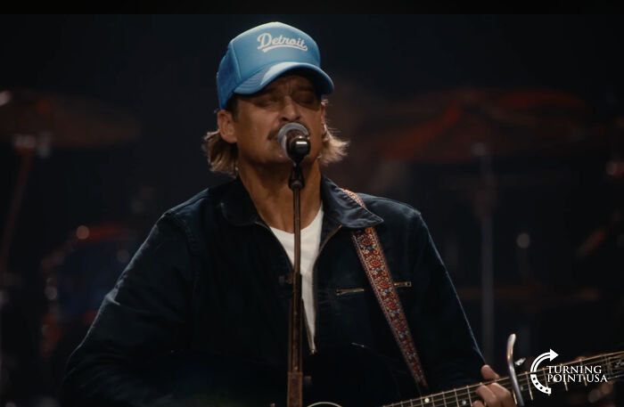 Man wearing a Detroit cap playing guitar and singing at a party with footage revealing Trump playing Bad Bunny music.