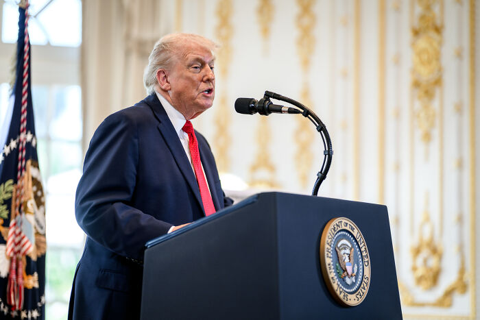 Man in suit speaking at podium with presidential seal, representing media and war on women themes.