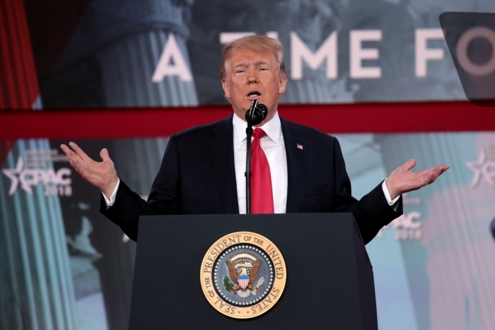 Donald Trump at a podium, speaking with hands open, discussing U.S. troops and Iranian oil tanker situations.
